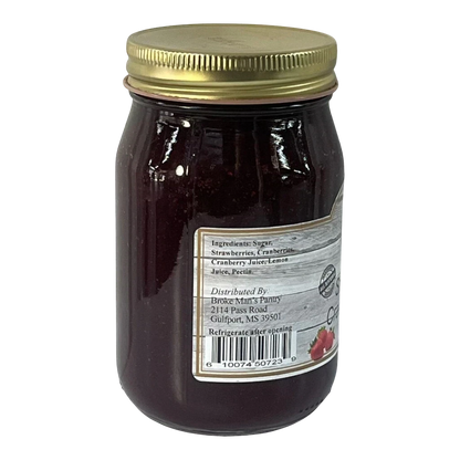 Broke Man's Pantry strawberry cranberry jam in a glass jar with a gold lid against a black background.